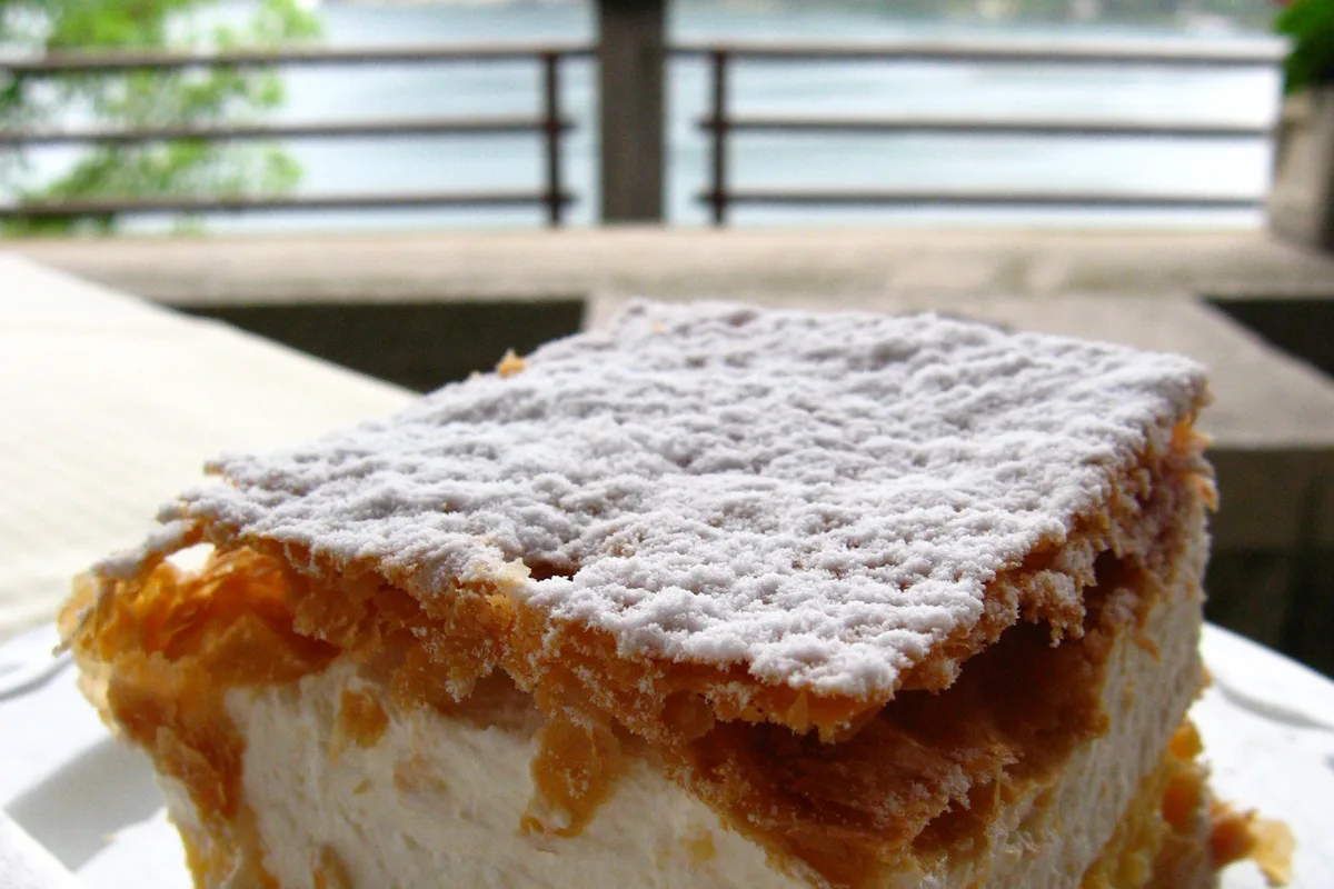 A slice of Bled cream cake on a café terrace, Bled Castle soft in the background