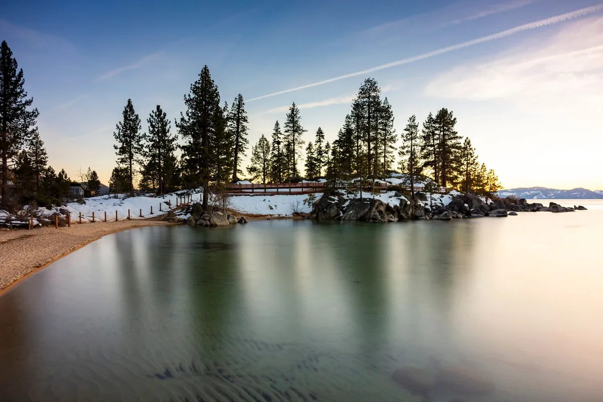 Sunset over a snowy Lake Tahoe shoreline, pines reflected in still water