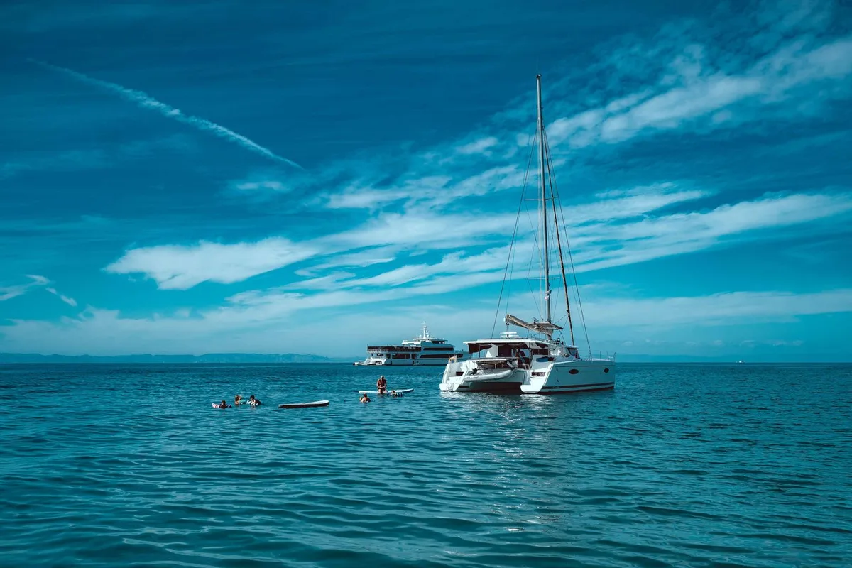 A catamaran at anchor in a turquoise cove while swimmers enjoy the water