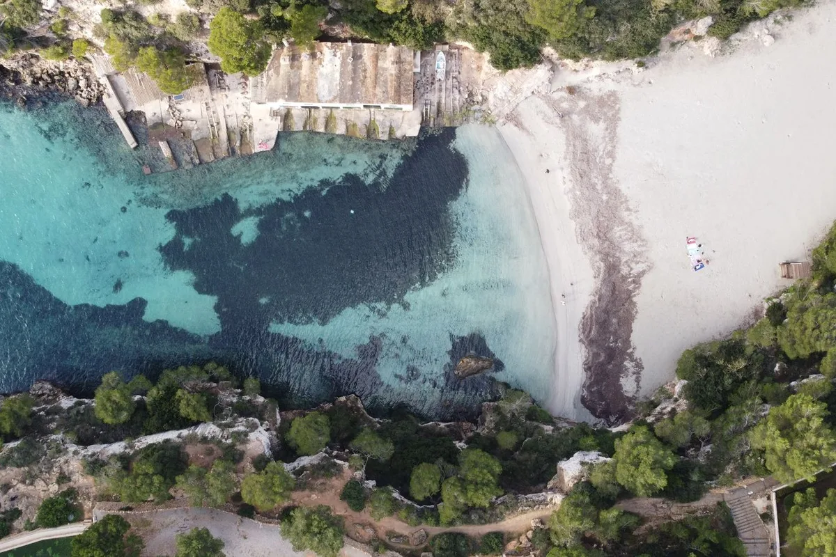 An aerial view of a white-sand cala with turquoise water on the Mallorca coast