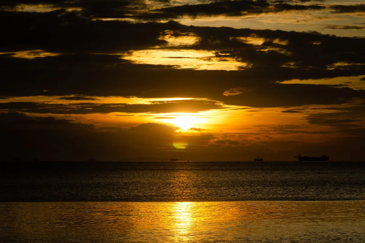 The sun setting over Manila Bay under heavy gold cloud