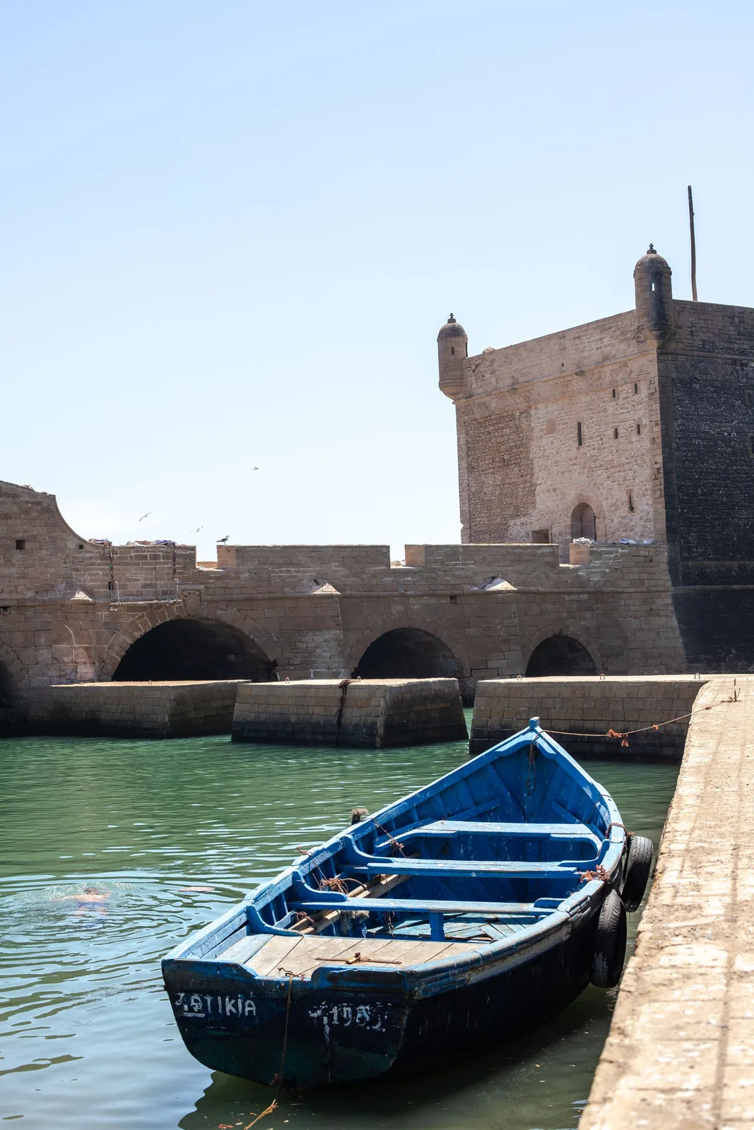 A blue fishing boat below Essaouira's harbour ramparts