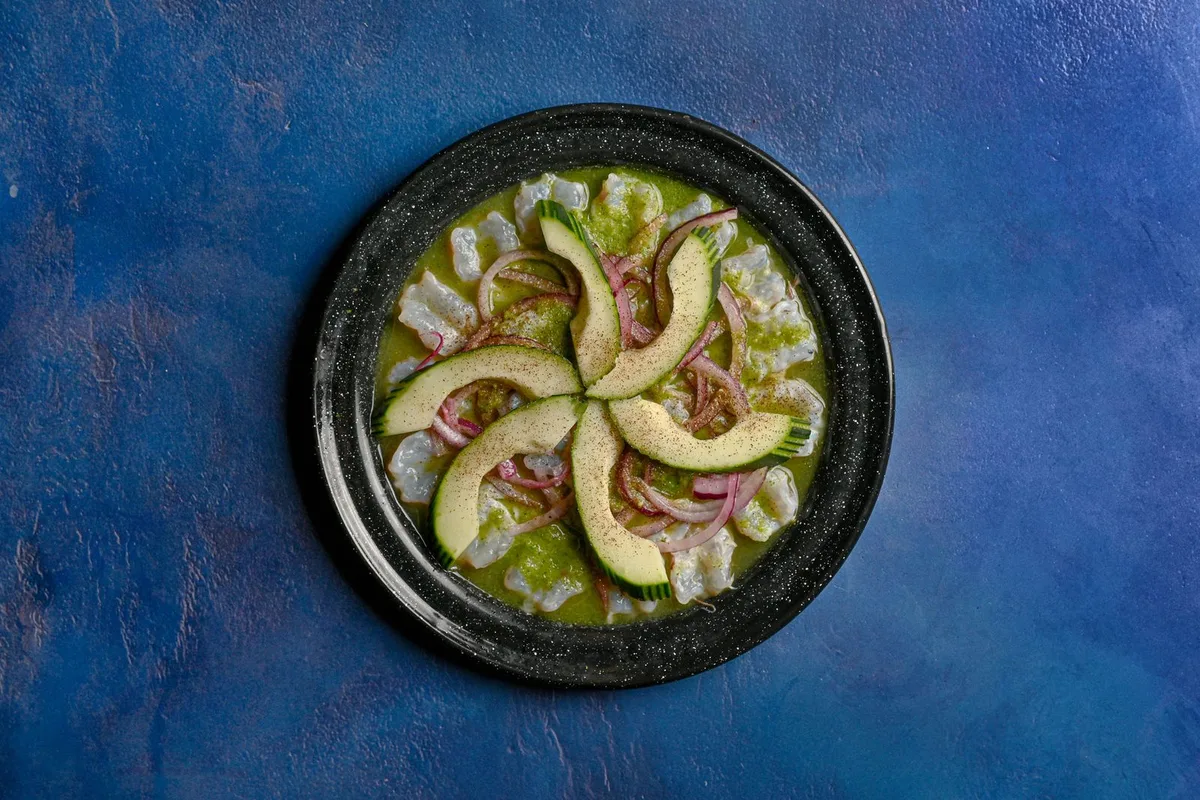 Aguachile, raw shrimp cured in lime and green chile, served with avocado on a dark plate