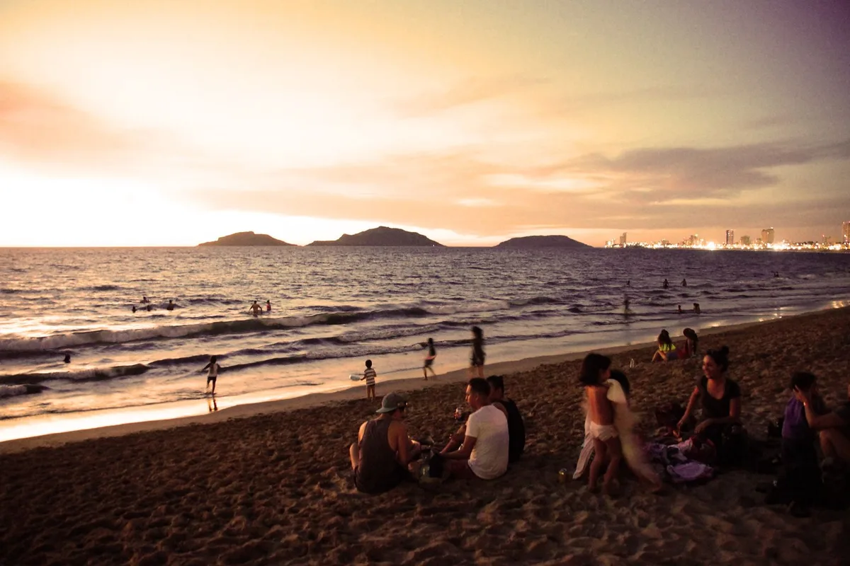 Sunset over a Mazatlán beach, people on the sand and the three islands offshore