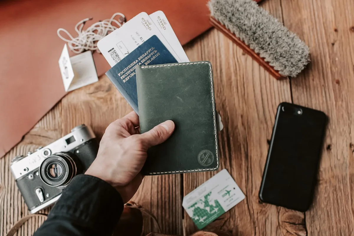A passport wallet with boarding passes, a camera and a phone on a wooden table