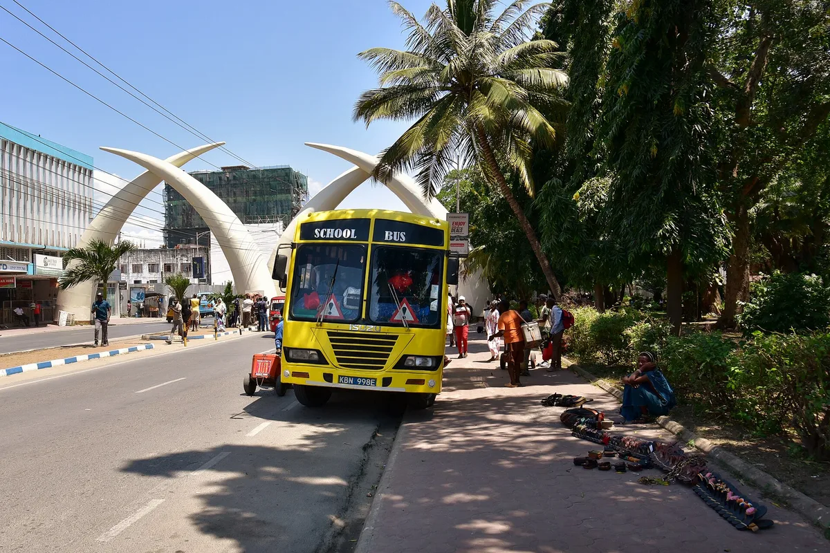 The Mombasa tusks spanning Moi Avenue, with a school bus passing beneath them