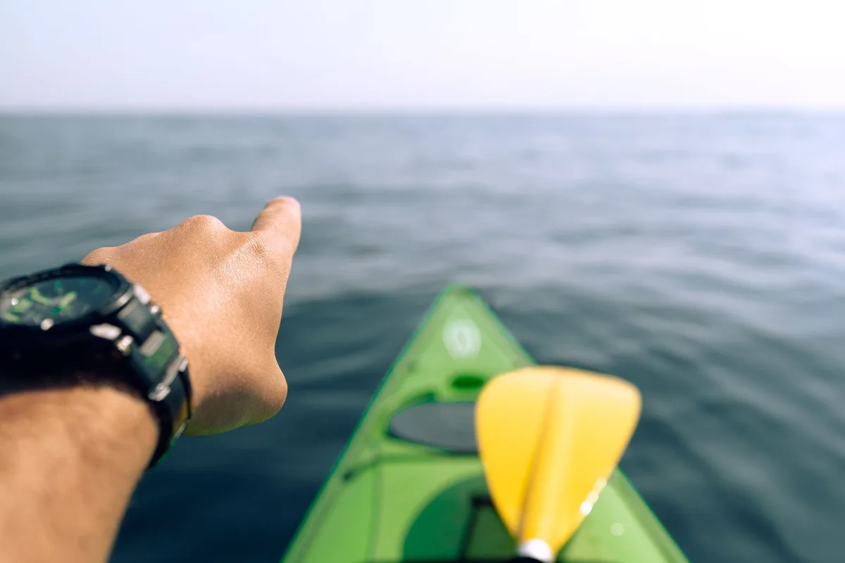 The bow of a green kayak and a paddle on the open water of Monterey Bay
