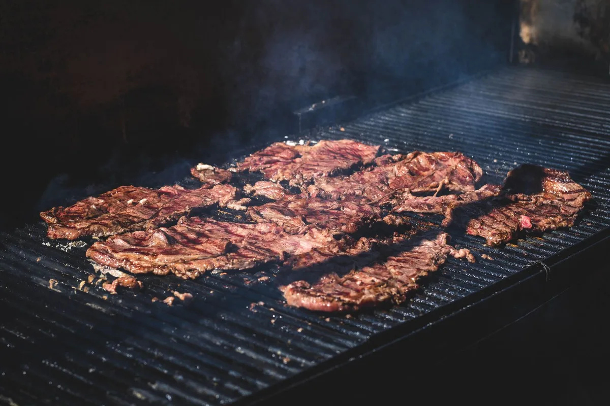 Thin-cut steaks grilling over the coals for a carne asada