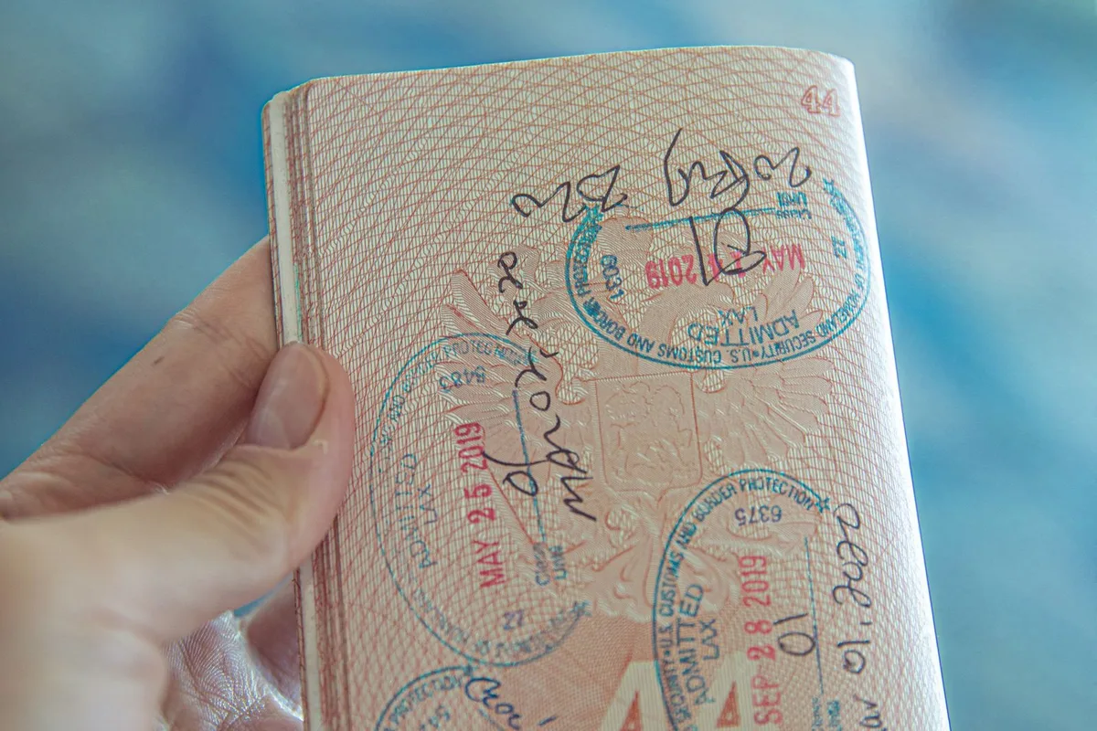 A hand holding a passport covered in entry stamps