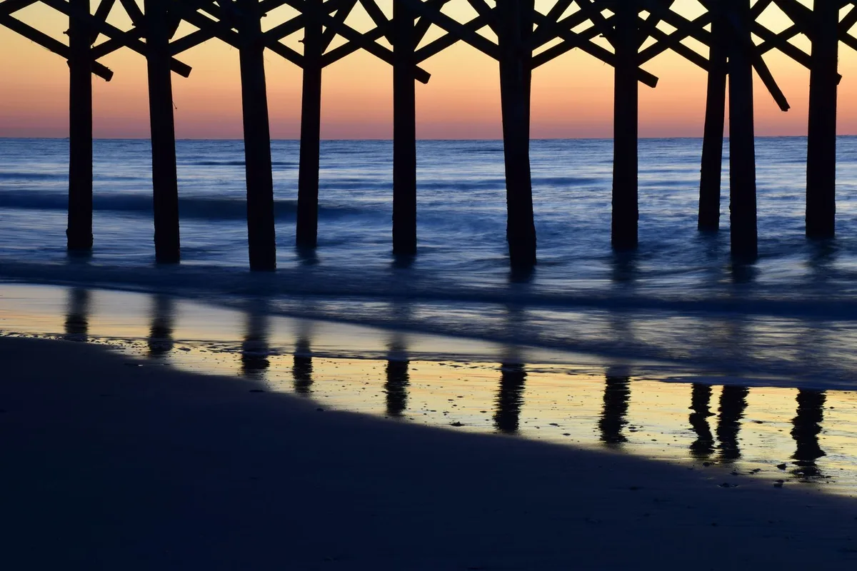 Sunset light under a Myrtle Beach pier, waves washing around the pilings