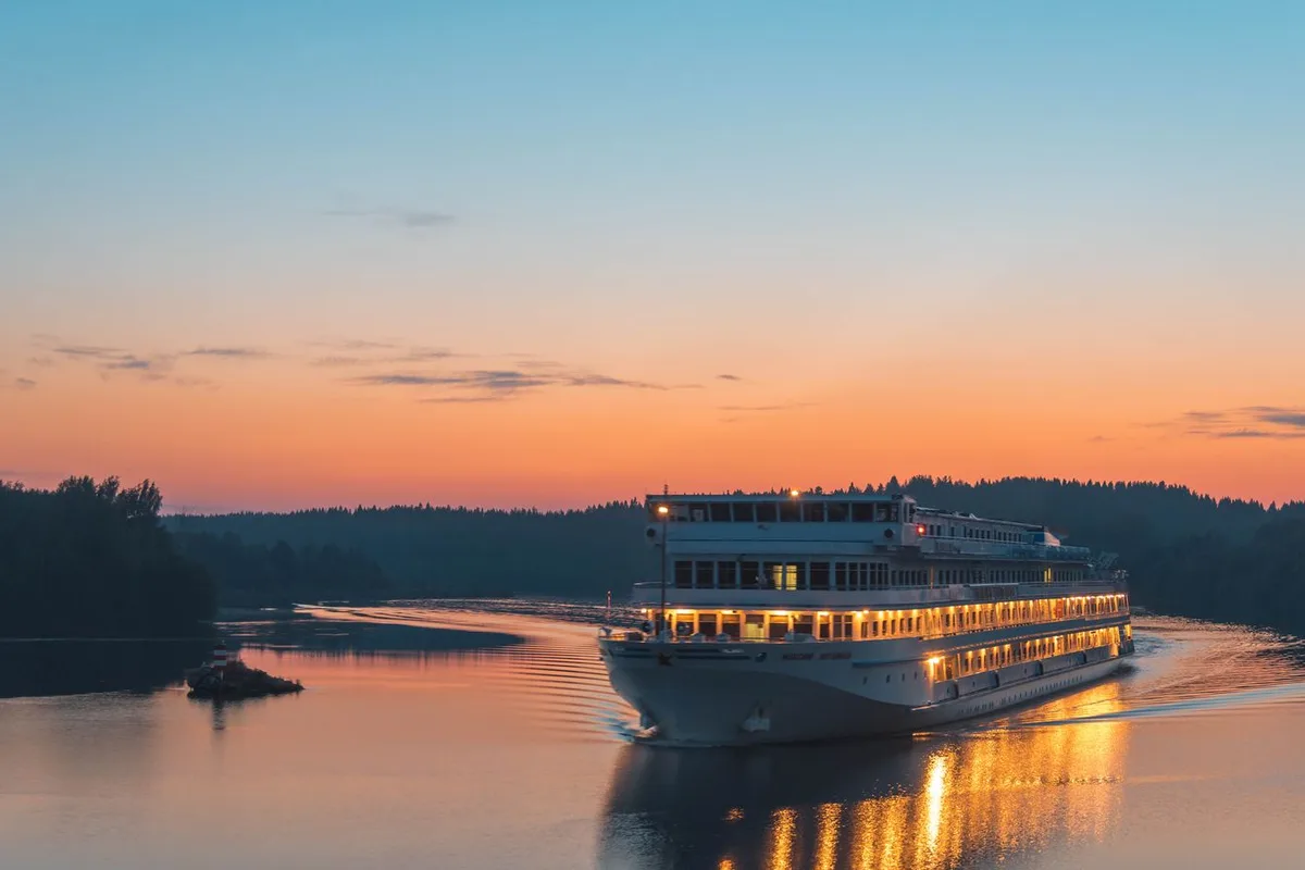 A cruise vessel lit up for the evening on calm water at sunset