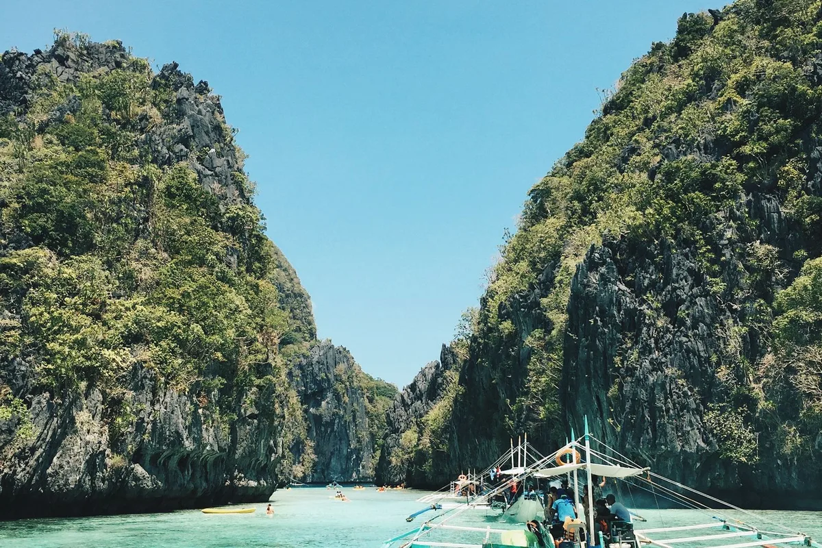 A bangka tour boat entering a lagoon channel between limestone cliffs in Bacuit Bay