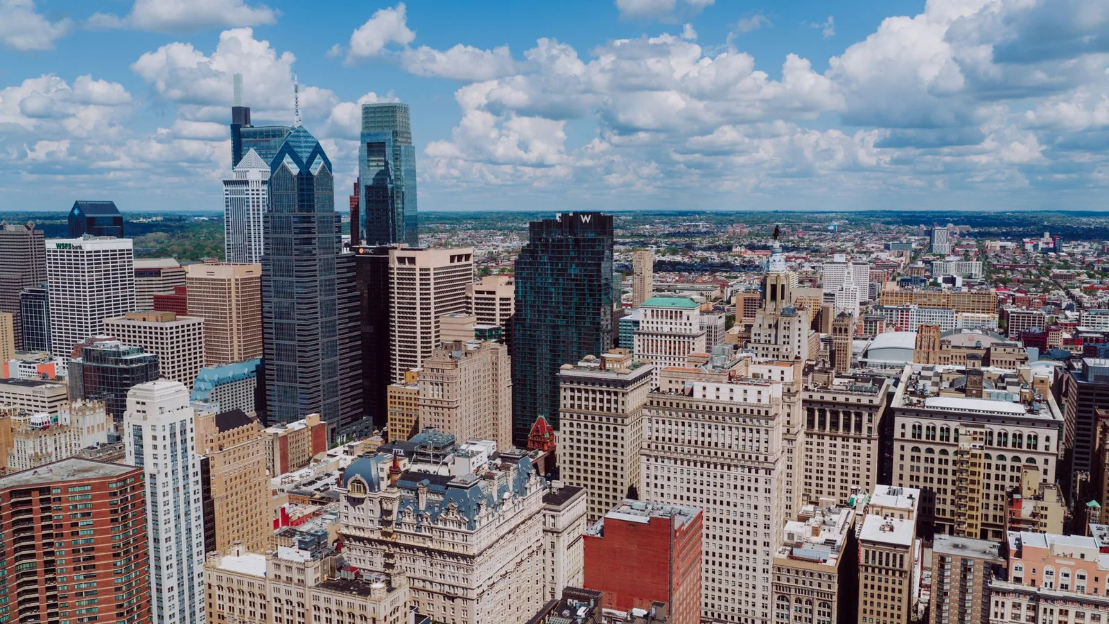an aerial daytime view over Center City rooftops toward One Liberty Place and City Hall