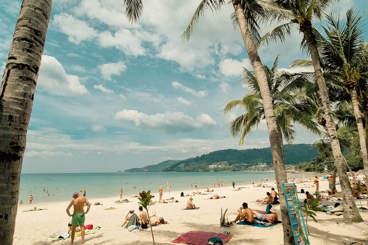 Palm trees over a busy Phuket west-coast beach with swimmers in the Andaman Sea