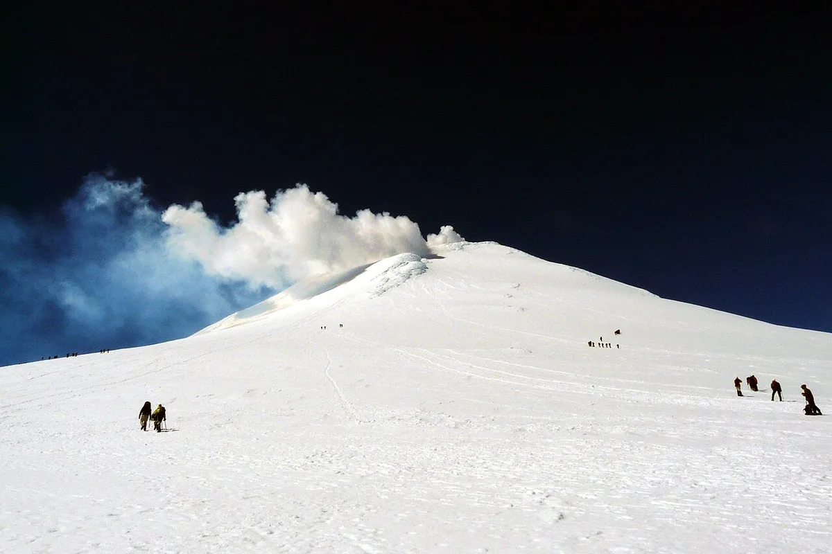 Climbers crossing the snow below the smoking crater of Villarrica volcano