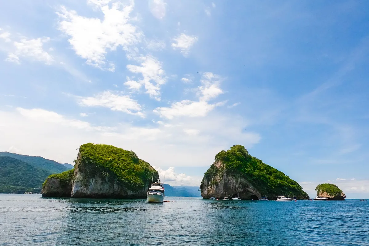 The granite islands of Los Arcos rising from a calm Banderas Bay, a tour boat alongside