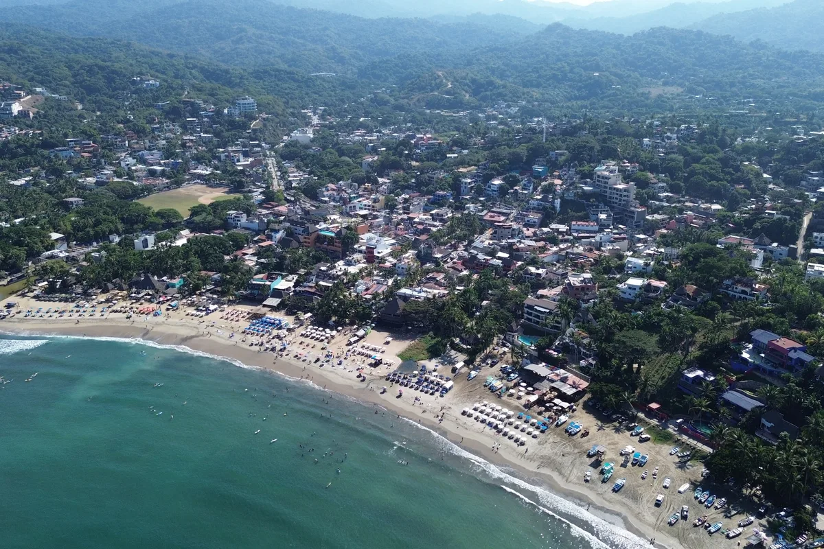 Sayulita from a drone, its surf beach curving under the green town