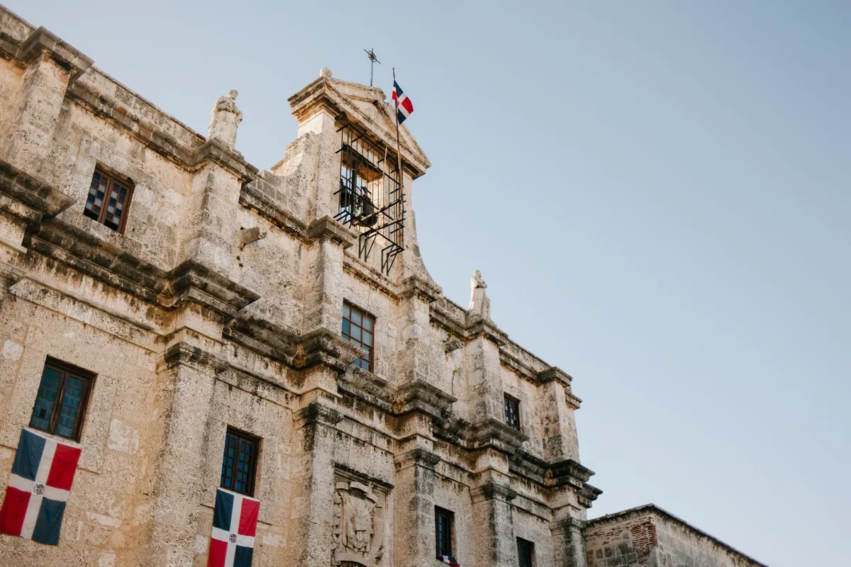 The stone facade of Santo Domingo's cathedral, Dominican flags flying above it