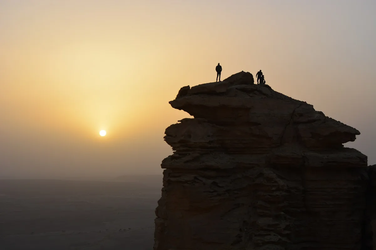 Hikers silhouetted on the rock pinnacle at the Edge of the World as the sun sets over the plain