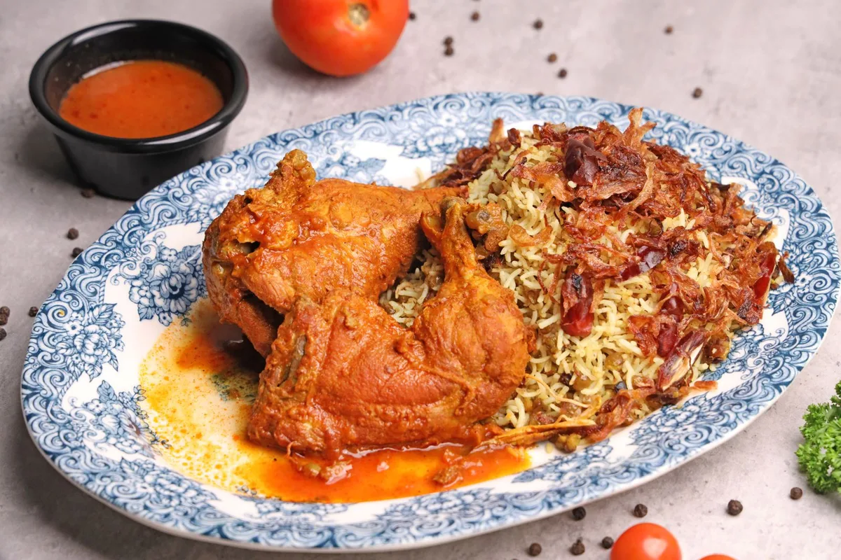 A platter of spiced chicken over fragrant rice, served kabsa style with a side of hot sauce