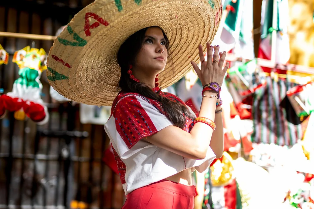 A market trader in a wide sombrero at a stall of colourful Mexican crafts