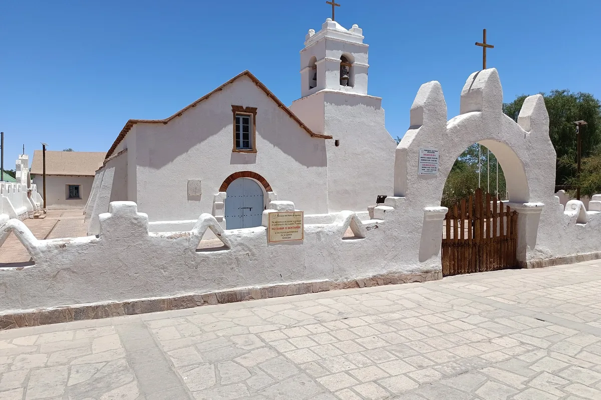The whitewashed adobe church of San Pedro de Atacama on the plaza, its bell tower against a desert-blue sky