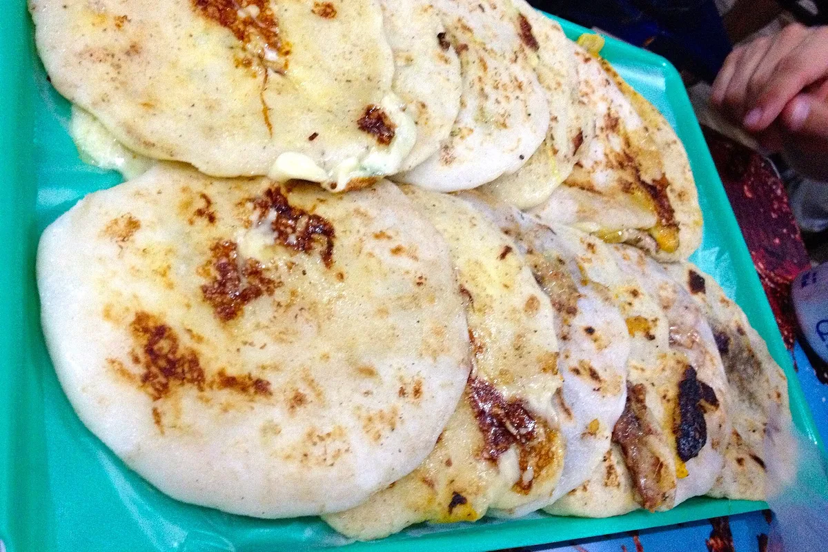 Pupusas browning on a tray in San Salvador, ready to eat with curtido and salsa