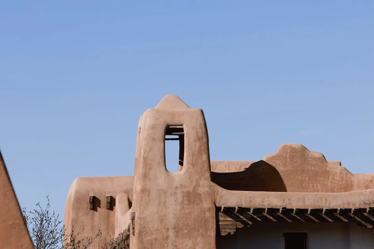 An adobe bell tower and Pueblo Revival rooftops in Santa Fe against a deep blue sky
