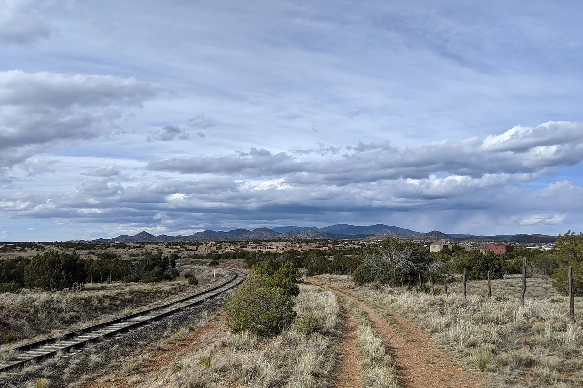 A rail line and dirt road crossing the high desert toward the Sangre de Cristo Mountains