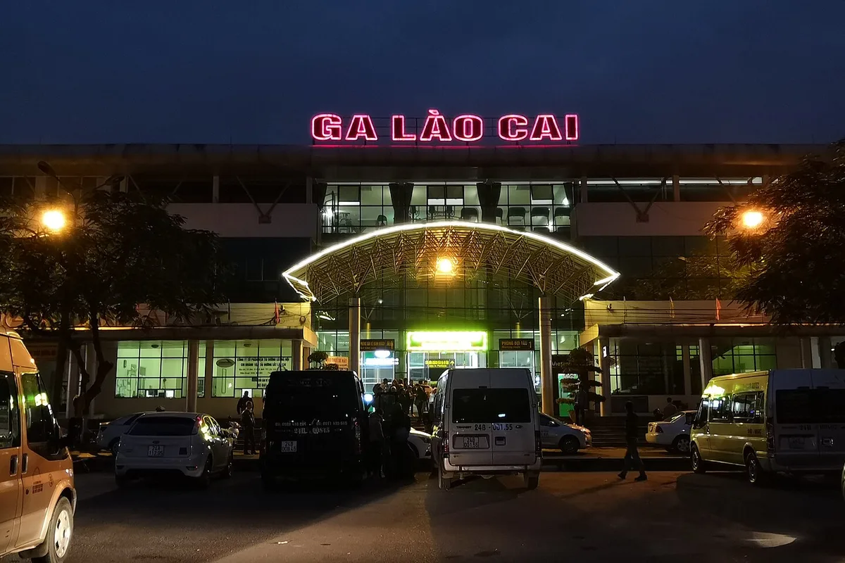 Lao Cai railway station at dusk, the neon Ga Lao Cai sign above the square and the minivans waiting outside