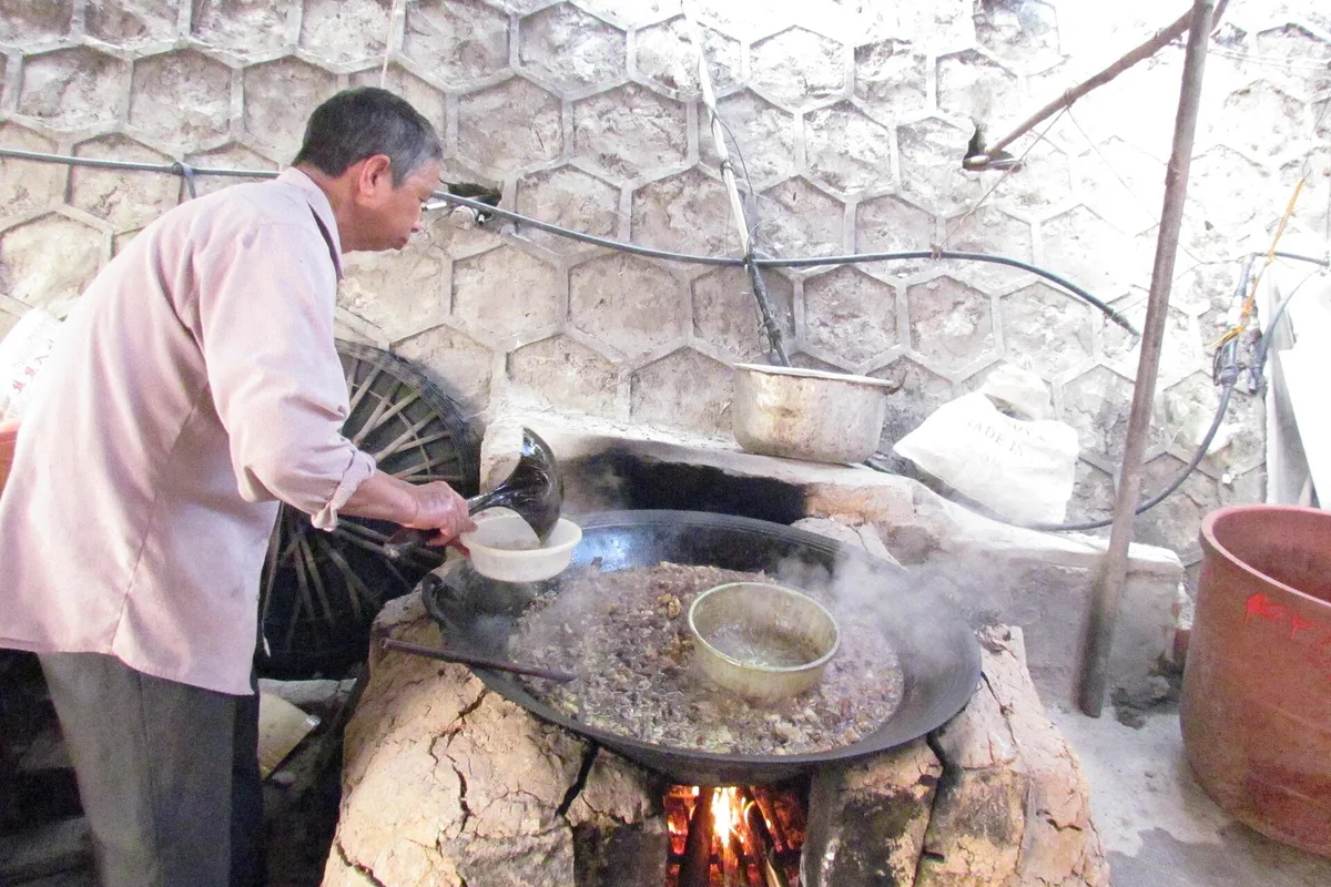 A cook stirring a wide pan of thang co over an open fire in Sapa