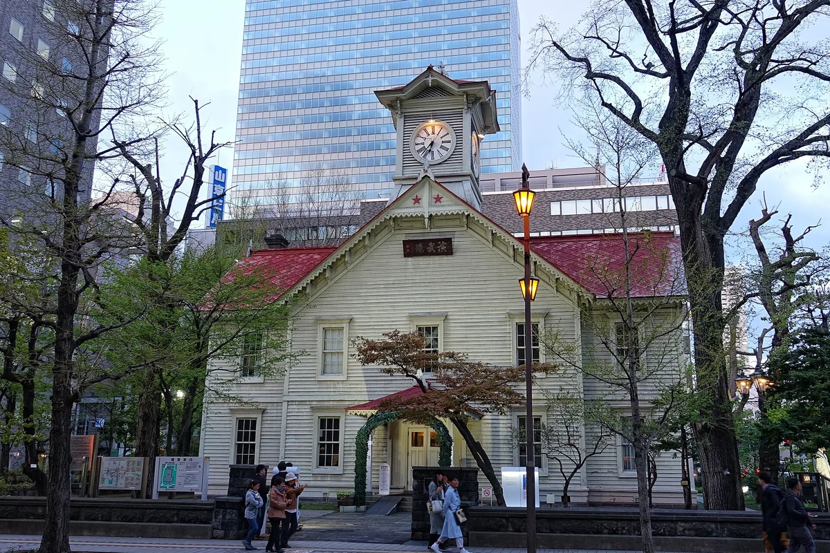 The Sapporo Clock Tower at dusk, its white wooden hall framed by trees