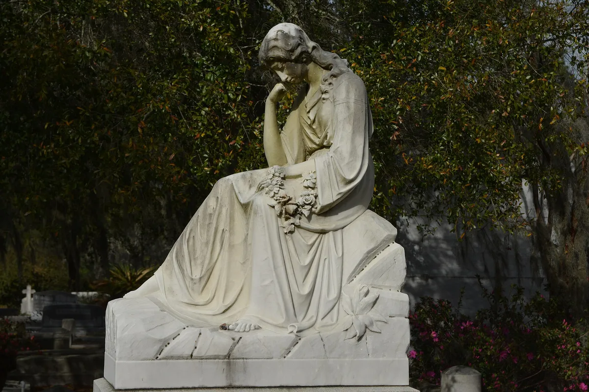 A weathered mourning statue among the graves at Bonaventure Cemetery