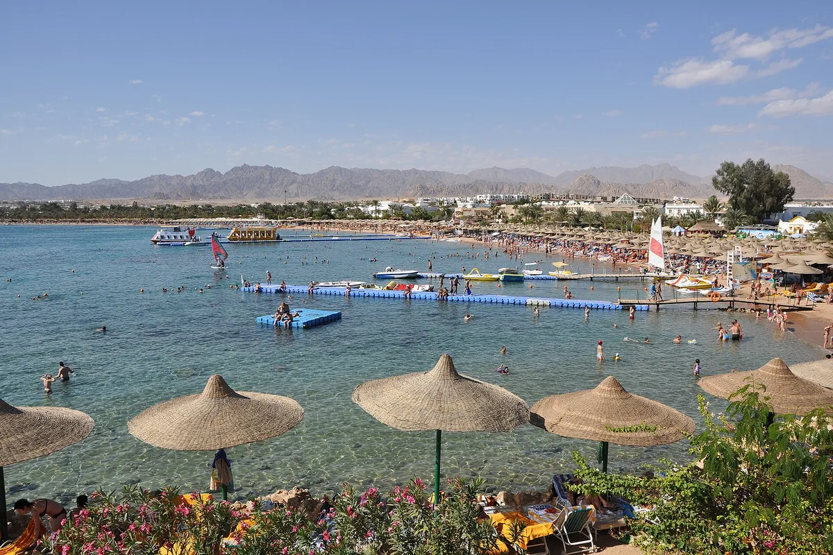 Naama Bay beach in Sharm el-Sheikh, umbrellas and bathers along the curving bay under the Sinai mountains