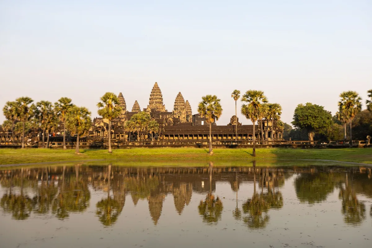 Angkor Wat and its five towers reflected in the reflecting pool, framed by palm trees