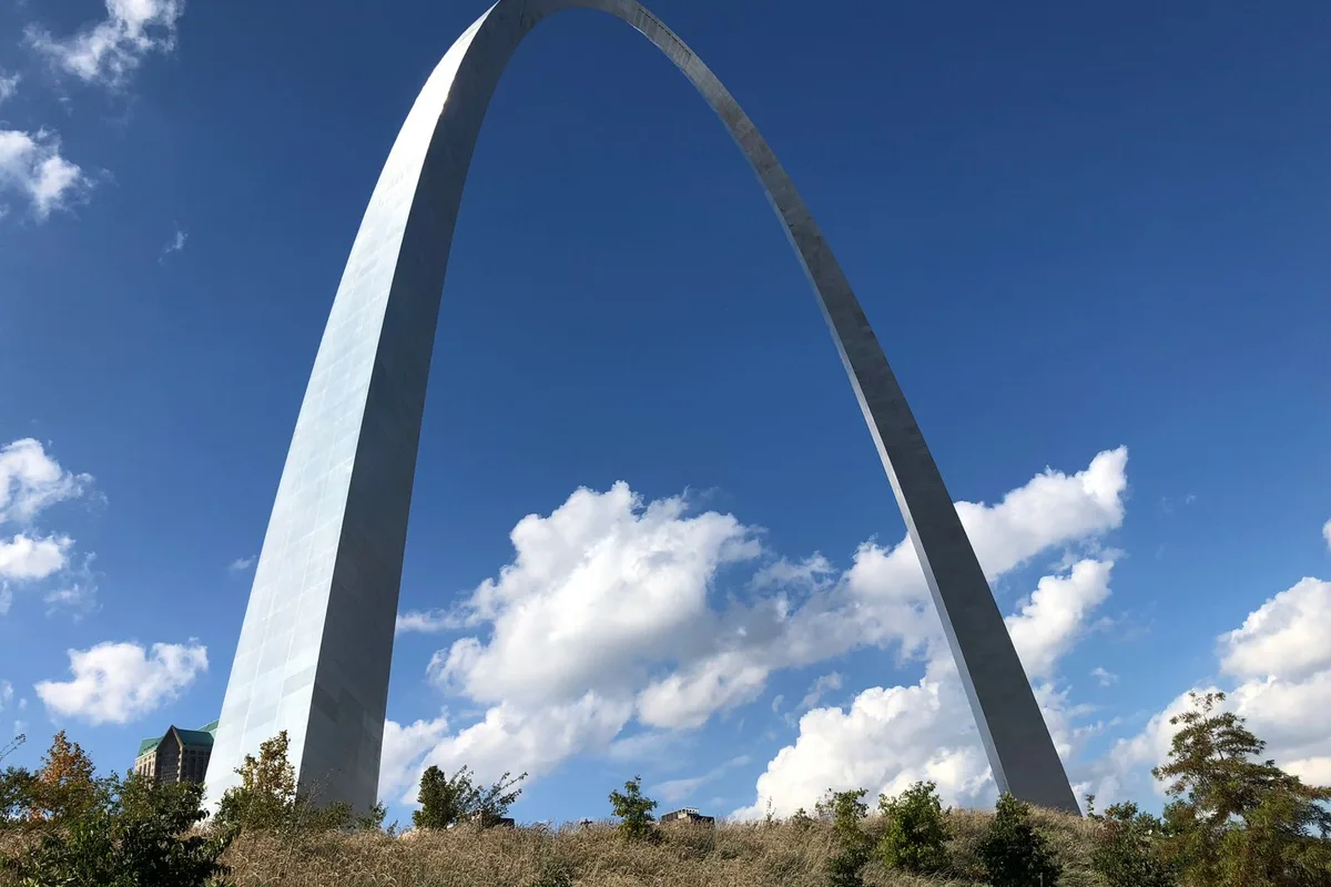 The Gateway Arch under a blue sky with white clouds, seen from its grounds