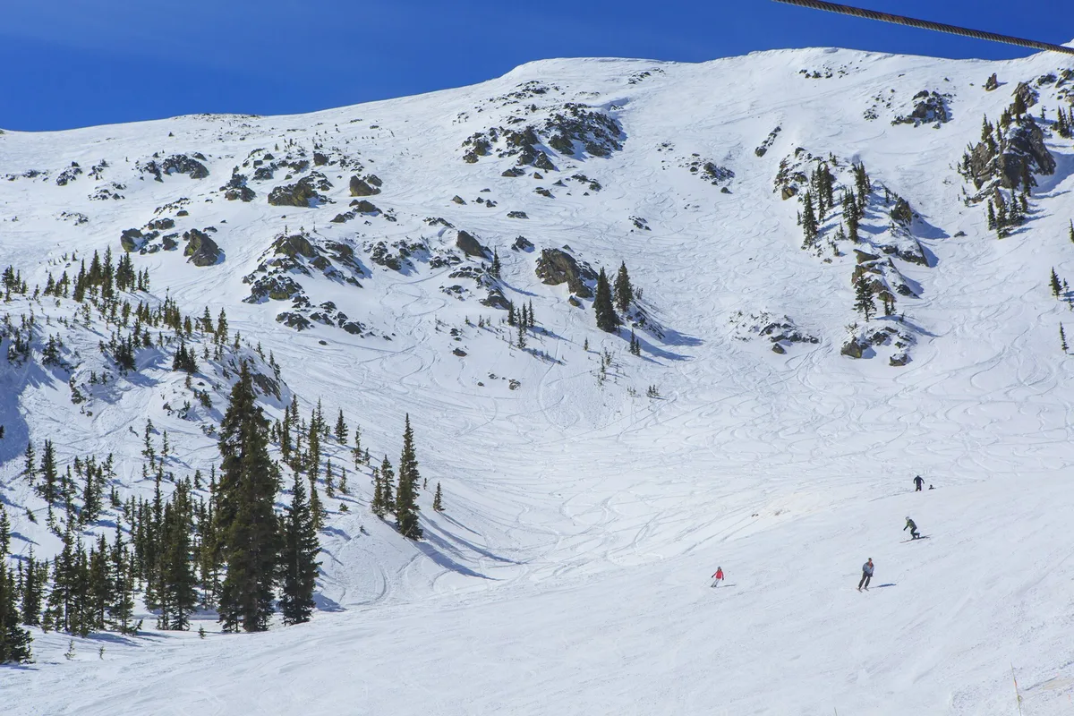Skiers on the snow-covered slopes of Taos Ski Valley under a blue sky