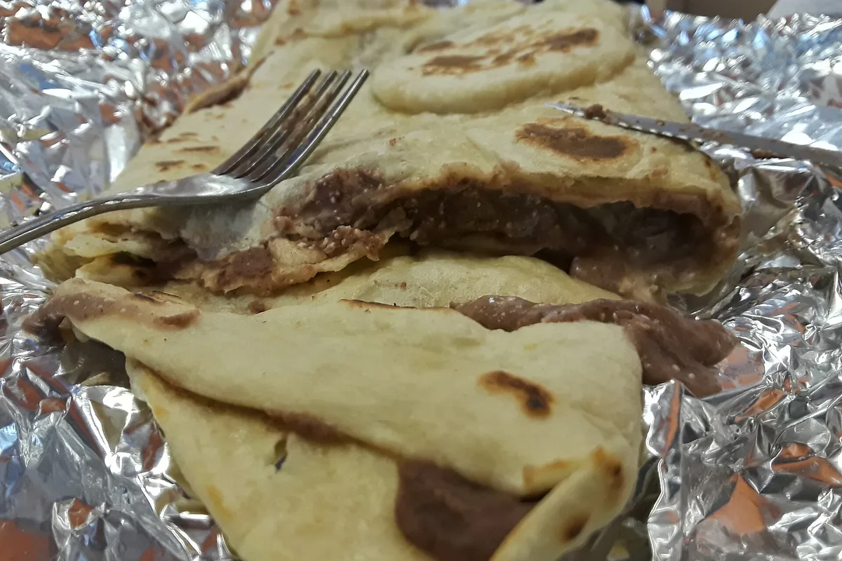 A baleada cut open, its flour tortilla folded around refried beans, cheese and crema