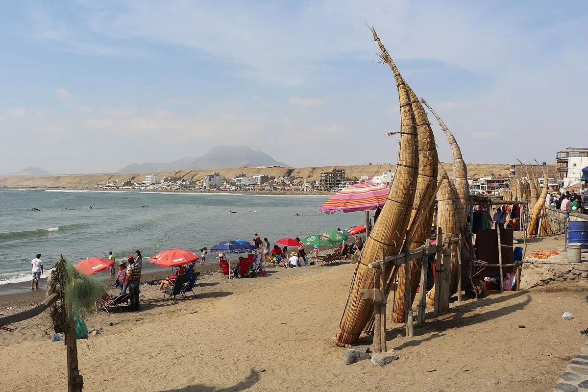 Caballitos de totora reed boats standing on the sand at Huanchaco beach, with swimmers behind