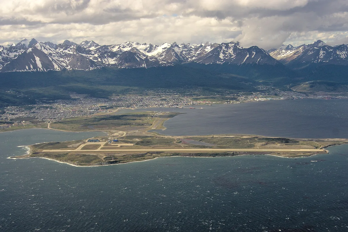 Ushuaia from the air — the airport peninsula in the bay, the city grid and the snow-capped Andes behind