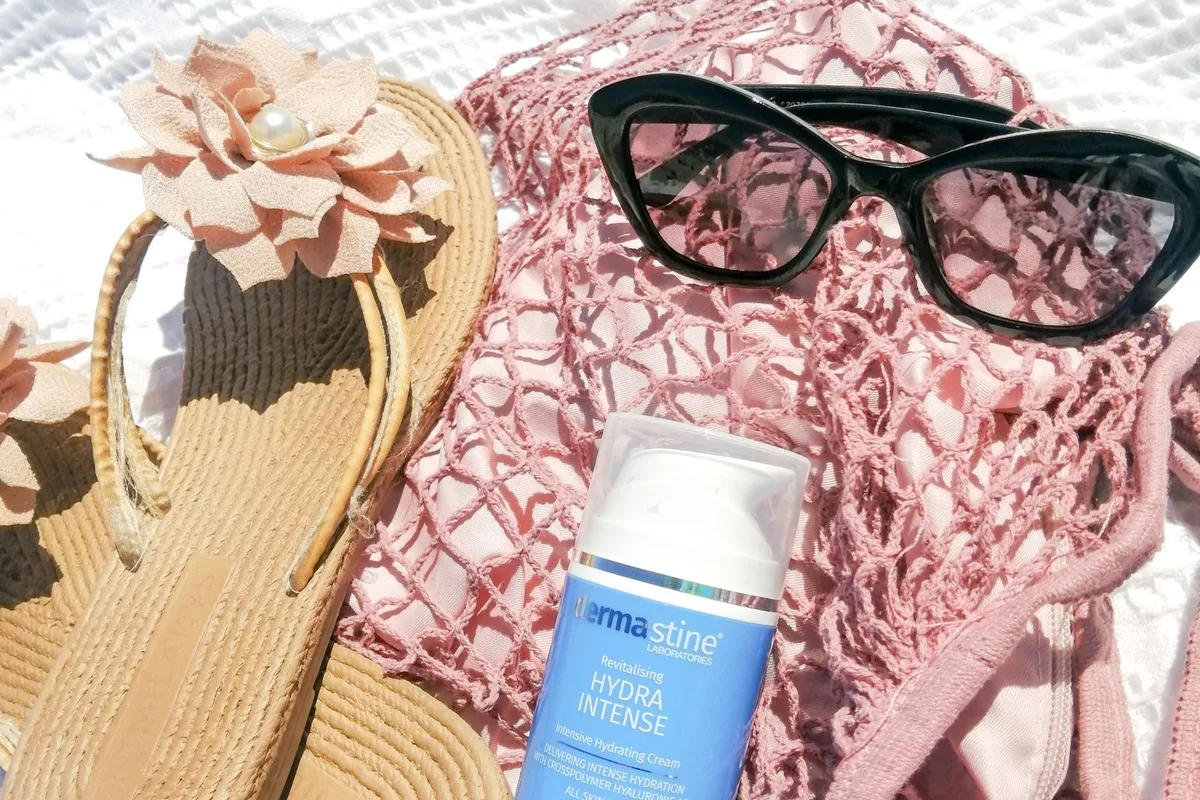 Beach-day gear on a towel — sunglasses, sandals and sun cream in a mesh beach bag