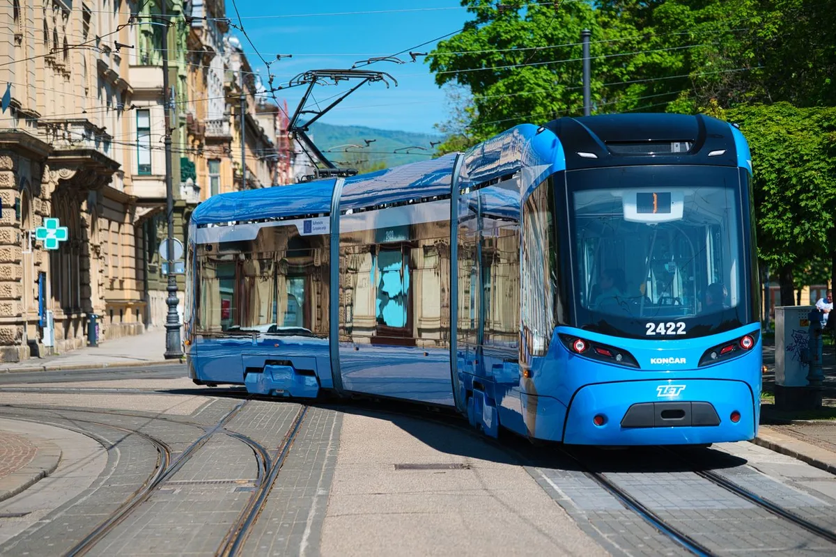 A blue ZET tram turning through a tree-lined Zagreb avenue