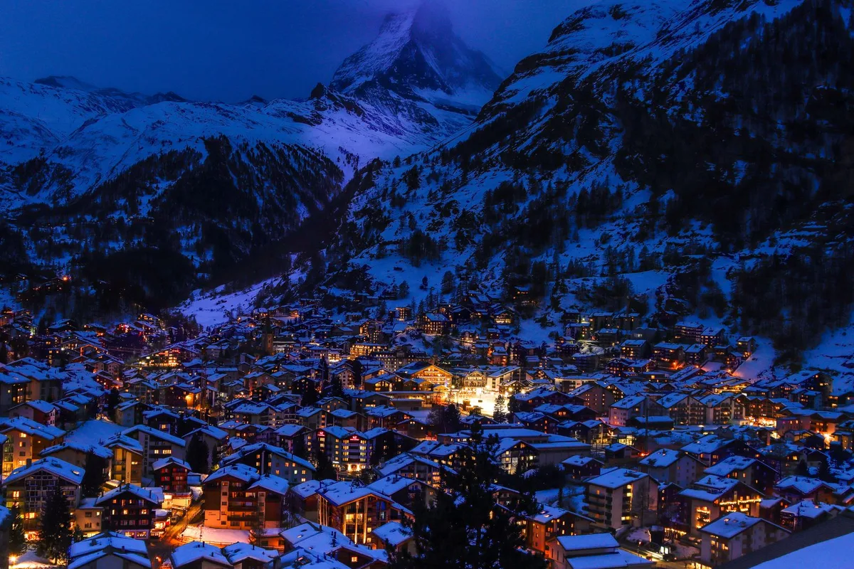 Zermatt at night, houses lit against snowy mountains